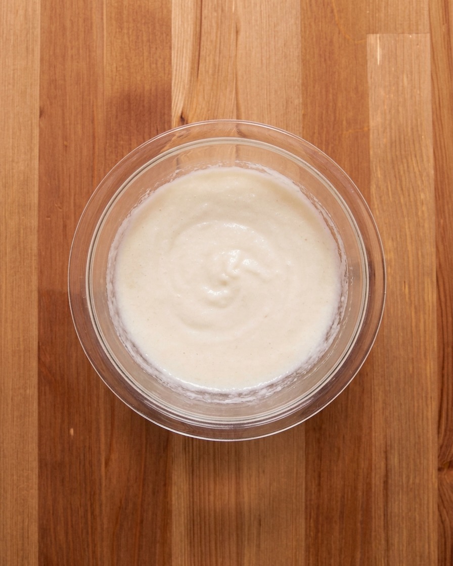 Die weiße Yamswurzel-Paste wird in einer Glasschale mit Brühe verrührt.