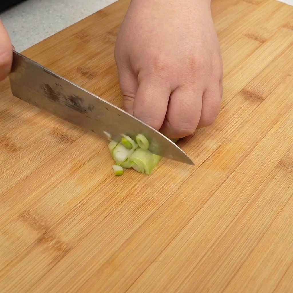 Fein gehackte Frühlingszwiebeln auf einem Holzschneidebrett.