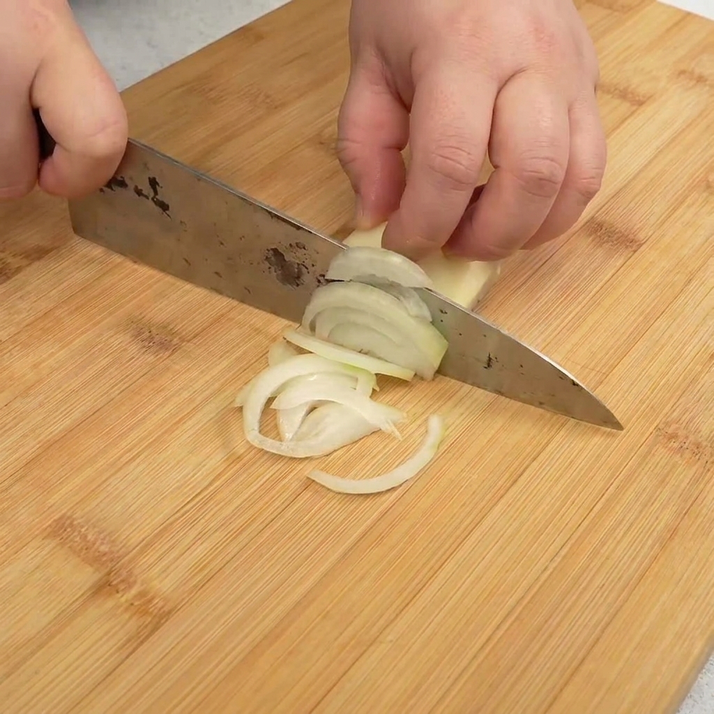 Dünn geschnittene weiße Zwiebelstreifen auf einem Holzschneidebrett.
