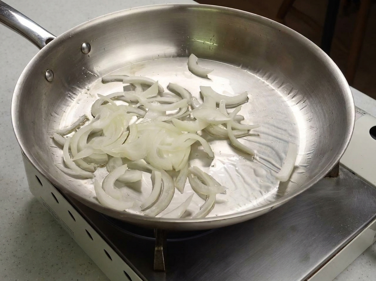 Weiße Zwiebelstreifen werden in einer glänzenden Edelstahlpfanne angebraten.