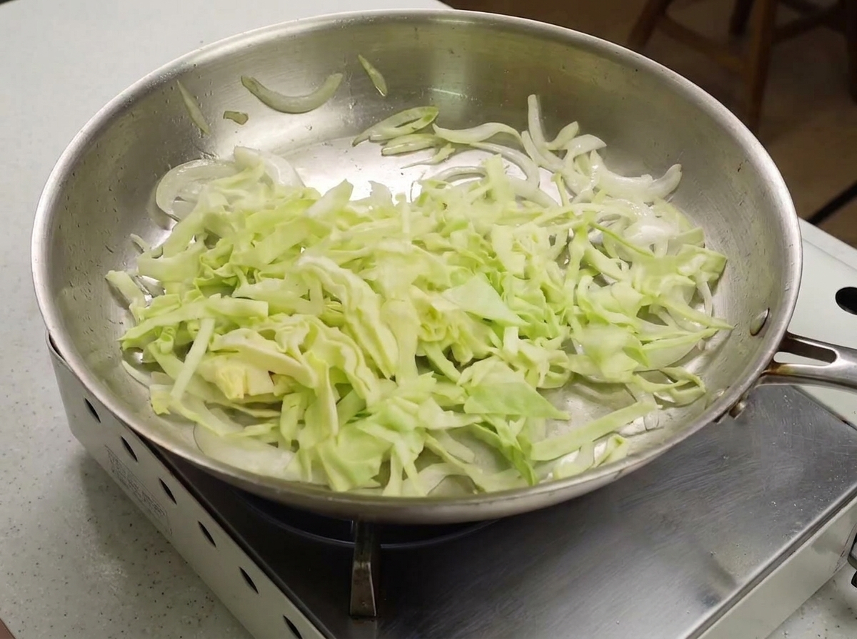 Fein geschnittener grüner Kohl wird zu den leicht angebratenen weißen Zwiebeln in die Pfanne gegeben.