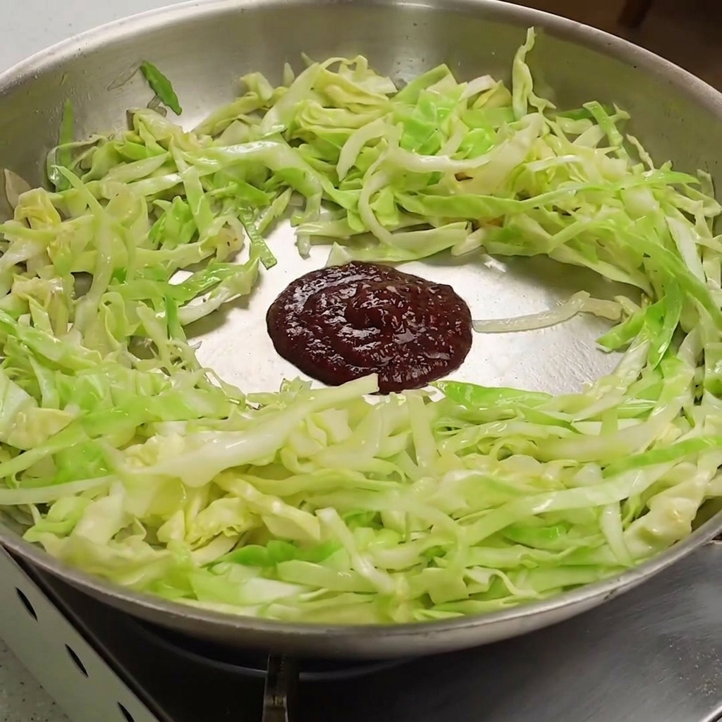 Ein dunkelroter Klecks gemischter Chili- und Sojabohnenpaste auf dem weich gedünsteten Kohl in einer Pfanne.