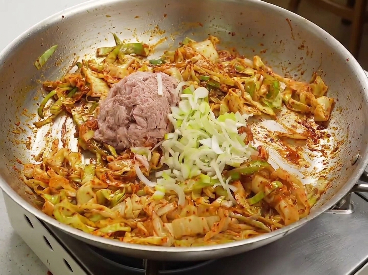 Aufgelockerter Dosen-Thunfisch und gehackte Frühlingszwiebeln auf der roten, mit Sauce überzogenen Kohlmischung in einer Pfanne.
