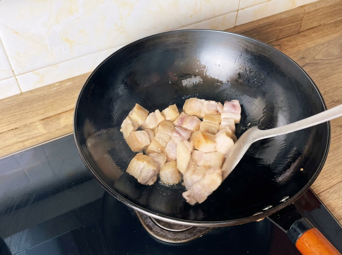 Schweinebauchwürfel werden in einem Wok mit einem Spatel goldbraun angebraten.
