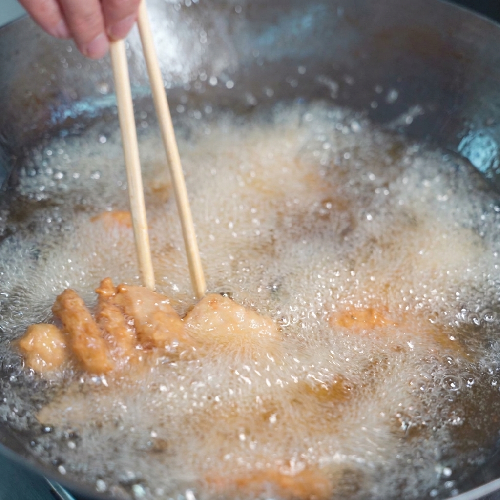 Panierte Fleischstücke braten im sprudelnden goldenen Öl und werden mit Holzstäbchen gewendet.