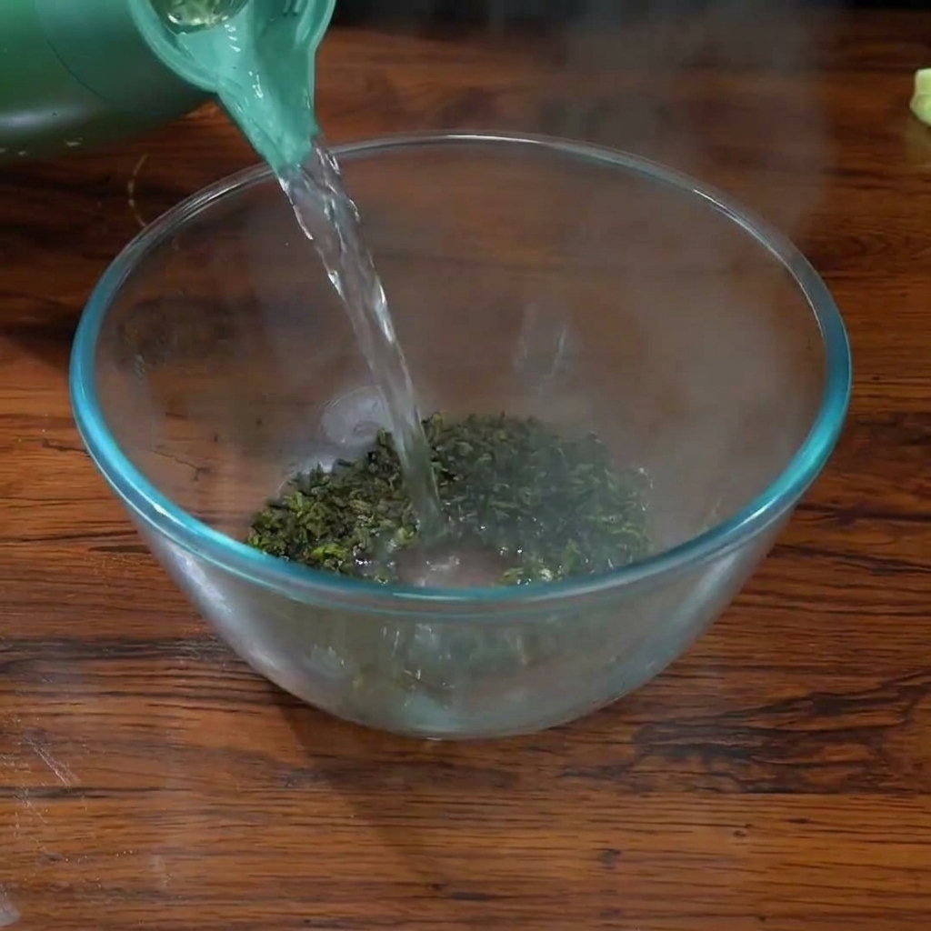 Kochendes Wasser wird aus einem grünen Wasserkocher über Tieguanyin-Teeblätter in einer Glasschale gegossen.