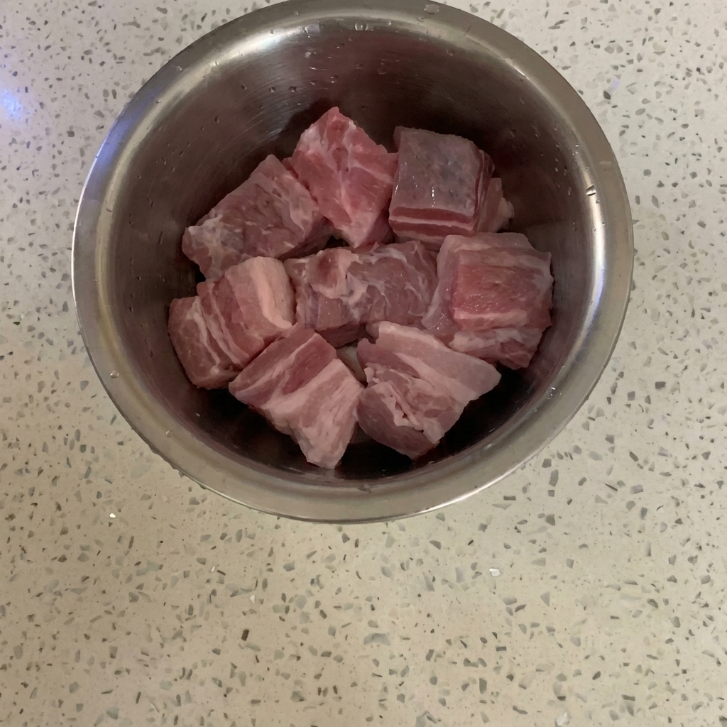 Rohe Schweinebauchwürfel in einer Edelstahlschüssel auf einer Arbeitsplatte.