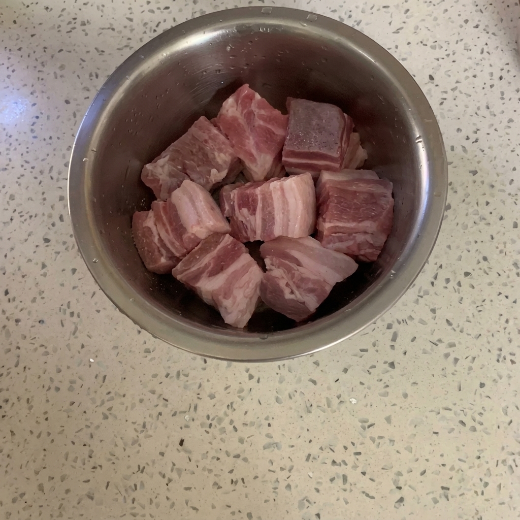 Eine Schüssel mit Schweinebauchwürfeln wird mit Pfeffer bestreut.