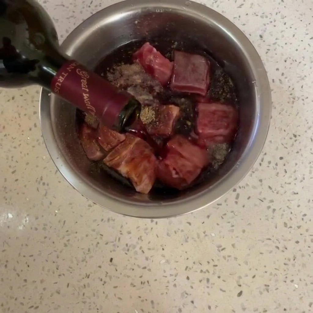 Rotwein wird über den Schweinebauch in einer Edelstahlschüssel gegossen.