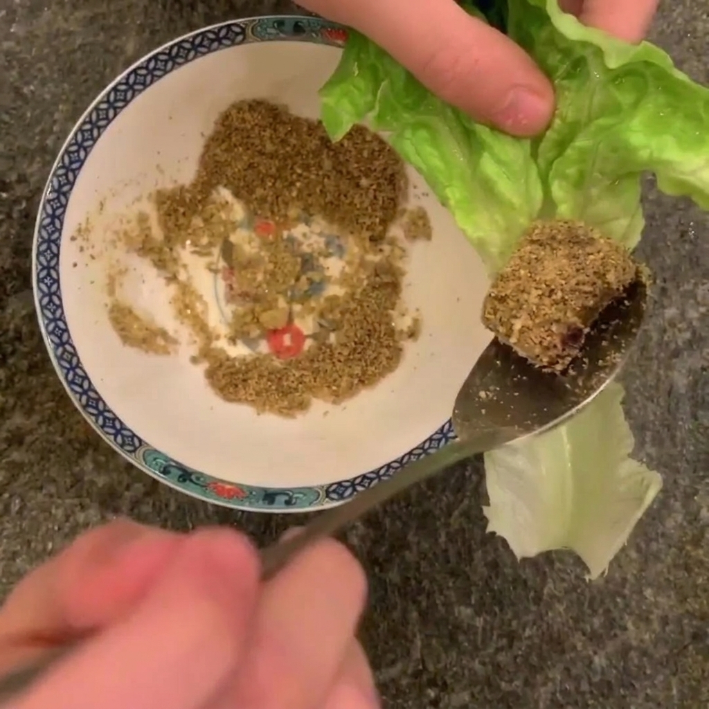 Ein Löffel hält ein Stück gebratenen Schweinebauch mit Erdnüssen über einem Salatblatt.
