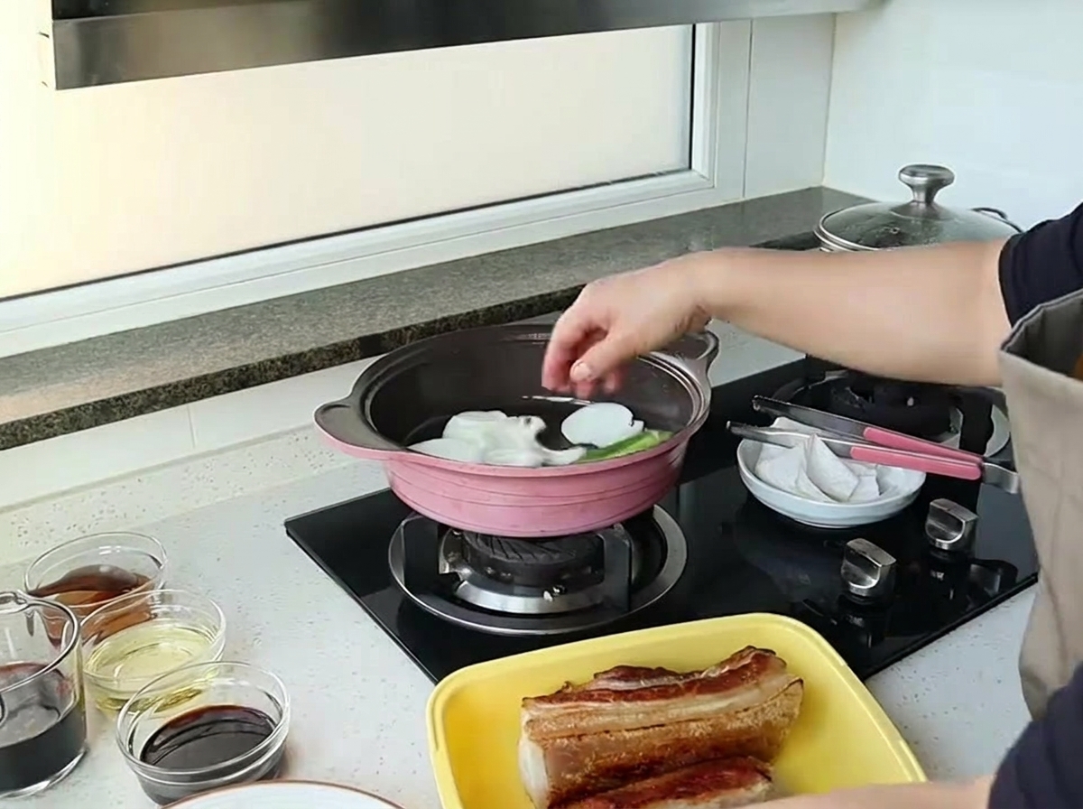 Eine Hand gibt große Zwiebelstücke in eine rosa Pfanne, um sie anzuschwitzen.
