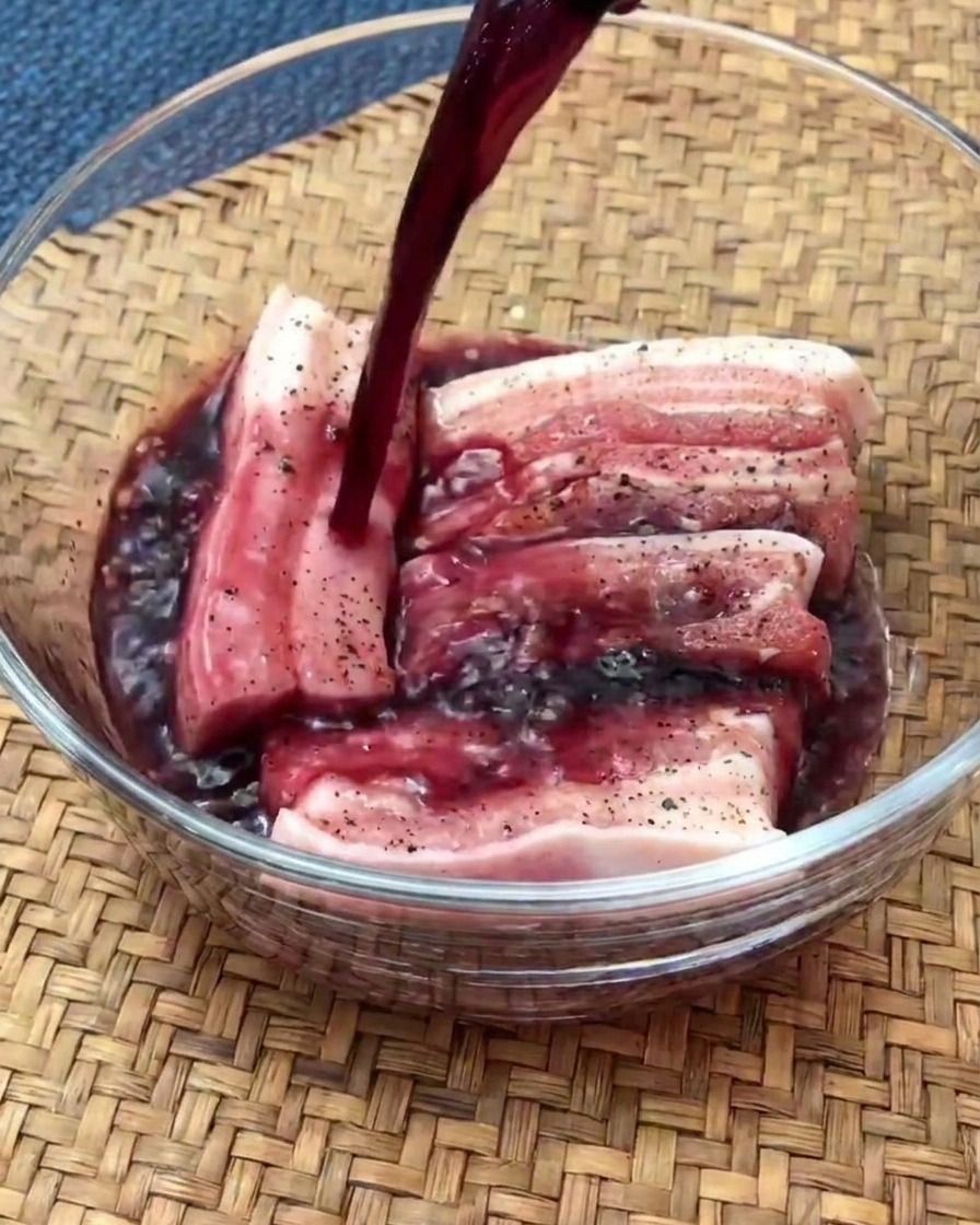 Rohe Schweinebauchscheiben, die in einer mit Rotwein gefüllten Glasschüssel marinierencite: 1.