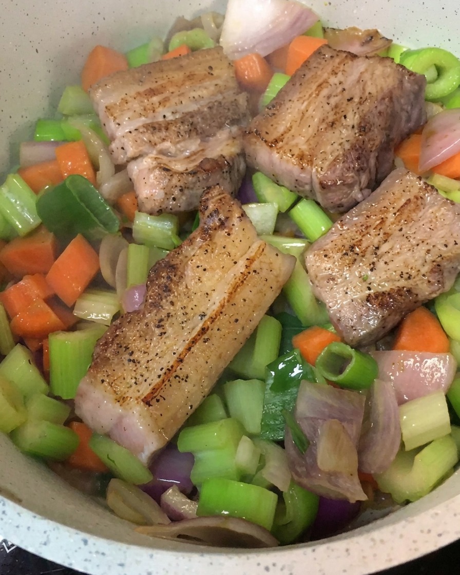 Angebratene Schweinebauchstücke, die auf einem Bett aus sautiertem Gemüse in einem Kochtopf liegencite: 1.
