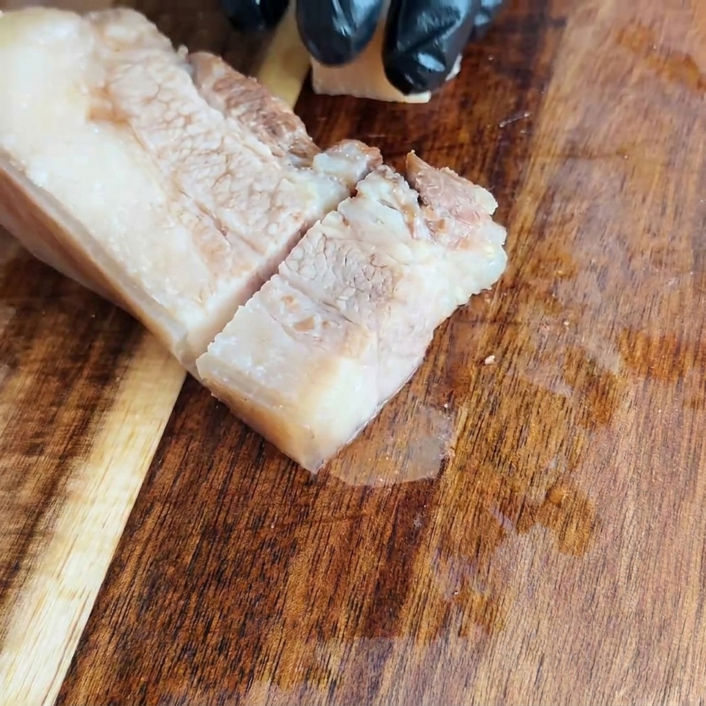 Abgekühlter Schweinebauch, der auf einem Holzbrett in gleichmäßige Quadrate geschnitten wird.