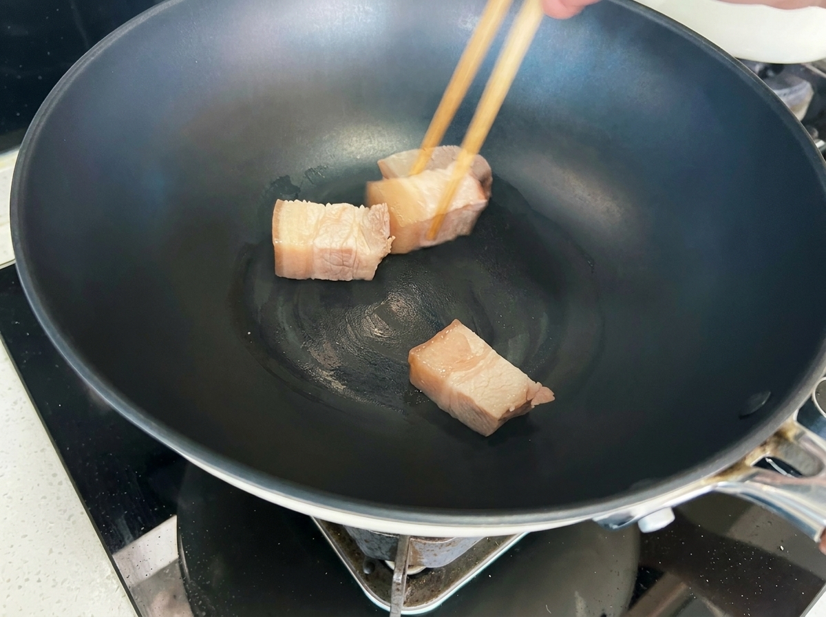 Schweinefleischwürfel werden in einem Wok goldbraun angebraten.