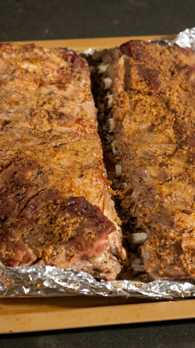 Zwei gegarte Schweinerippchen-Stränge liegen auf einem Backblech, die Alufolie wurde geöffnet und gibt den Blick auf das Fleisch frei.