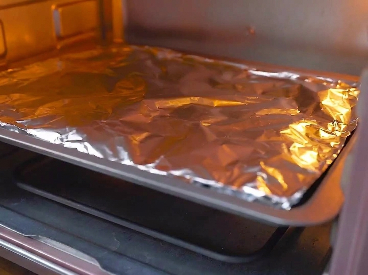 Ein mit Folie abgedecktes Backblech wird auf die mittlere Schiene eines vorgeheizten, glühenden Ofens geschoben.
