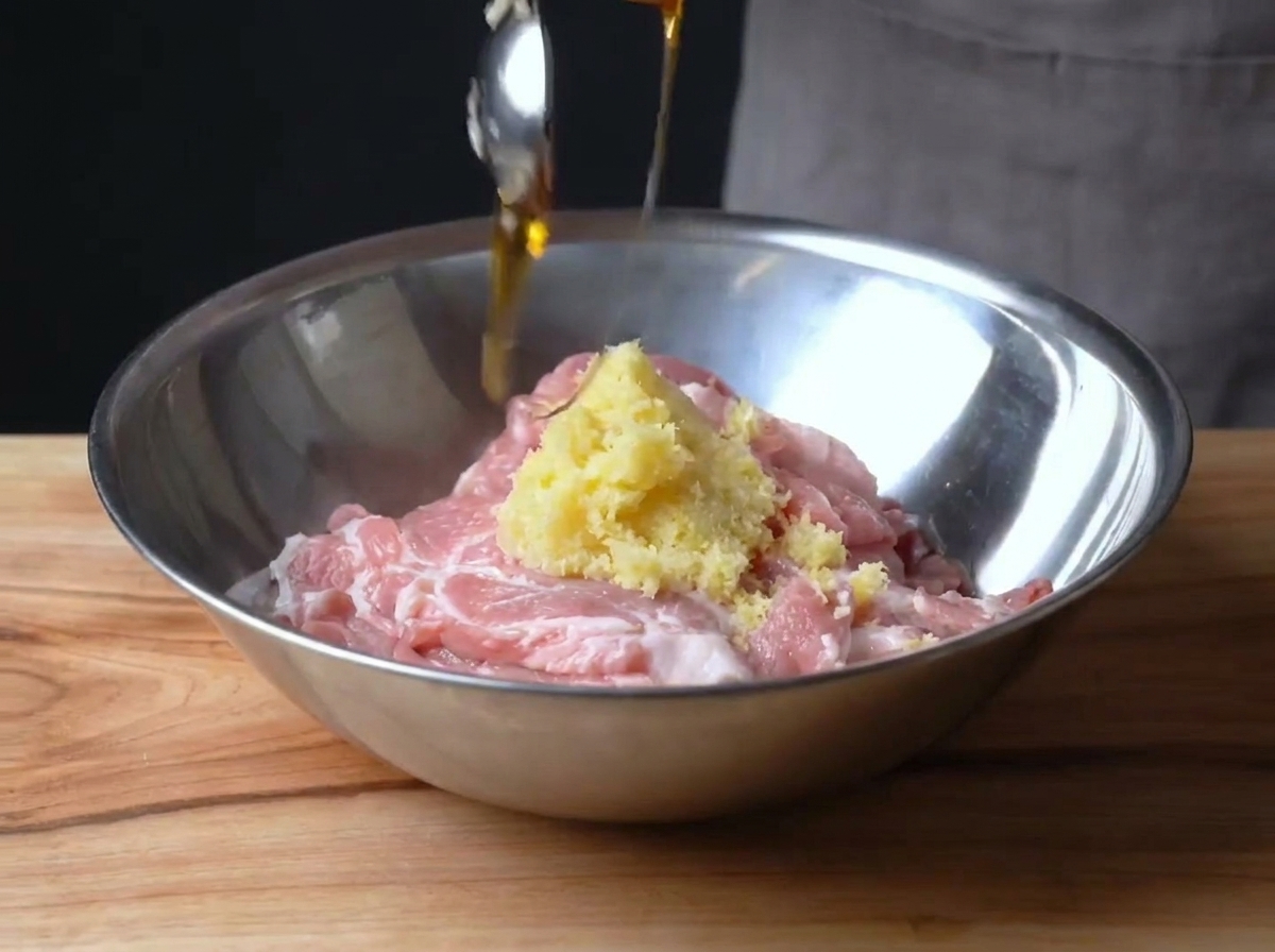 Rohes, in Scheiben geschnittenes Schweinefleisch in einer Metallschüssel, das mit Zitronenabrieb und Maissirup vermischt wird.
