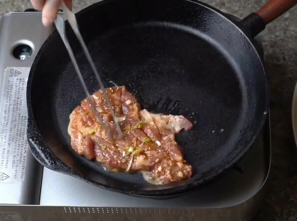 Ein einzelnes Stück des gewürzten, marinierten Schweinefleischs wird in eine vorgeheizte schwarze gusseiserne Pfanne gelegt.