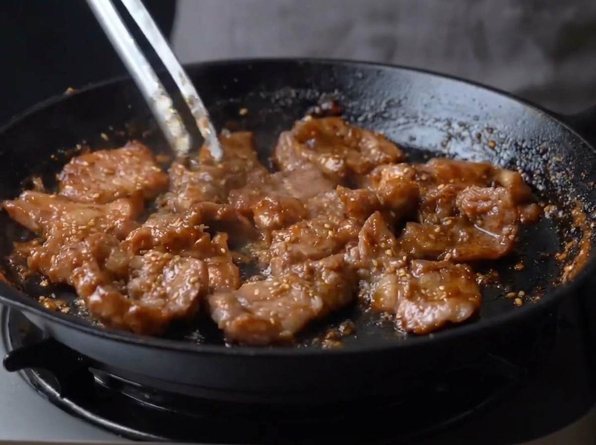 Mundgerechte Schweinefleischstücke werden in einer Pfanne umgerührt, überzogen mit einer dicken, glänzenden, dunkelbraunen karamellisierten Glasur.