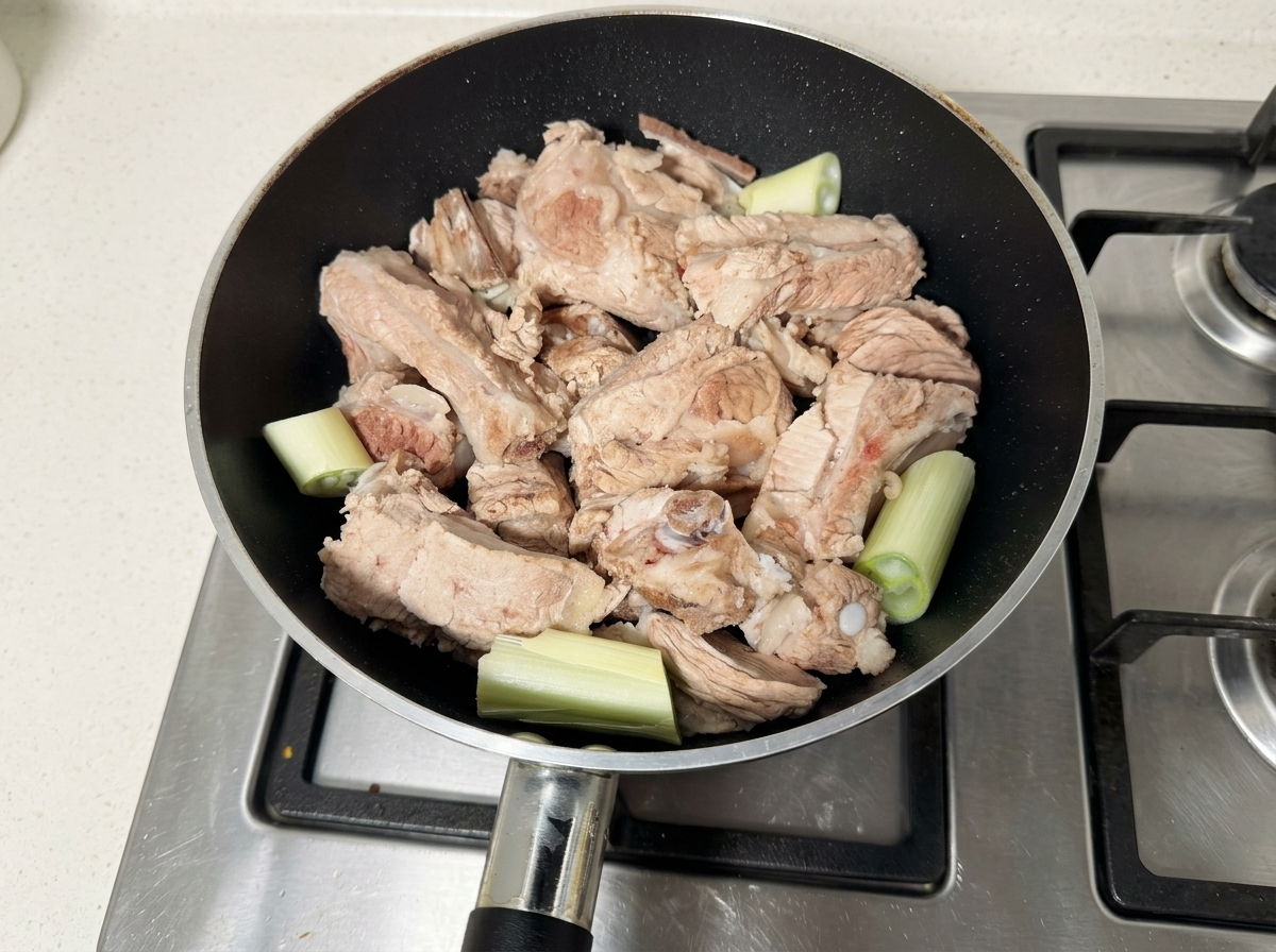 Rohe Schweinerippchen und Frühlingszwiebelstücke in einer schwarzen Pfanne.