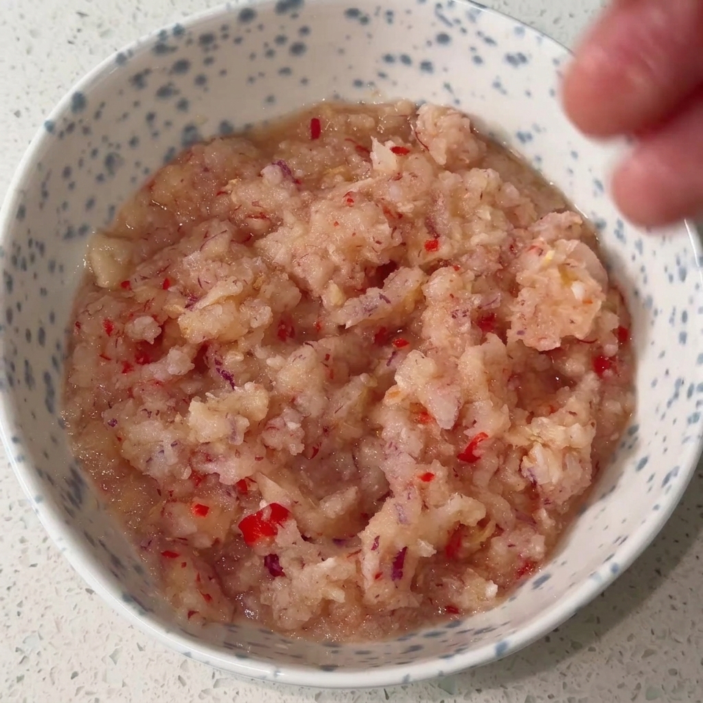 Eine Schüssel mit einer pürierten Zwiebel-Chili-Basis, die mit flüssigen und pulverförmigen Gewürzen vermischt wird.