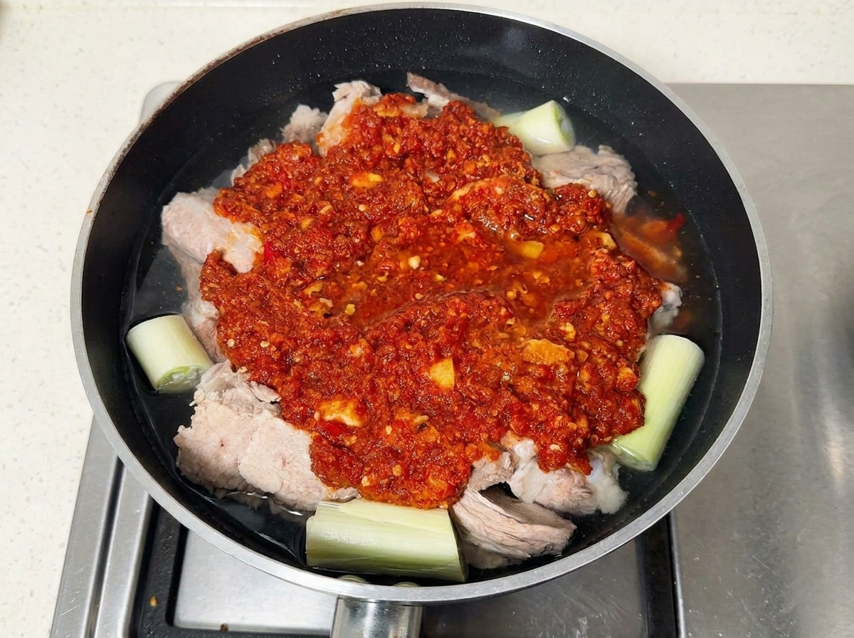 Schweinerippchen mit roter Chilipaste in einer mit Wasser gefüllten Pfanne.