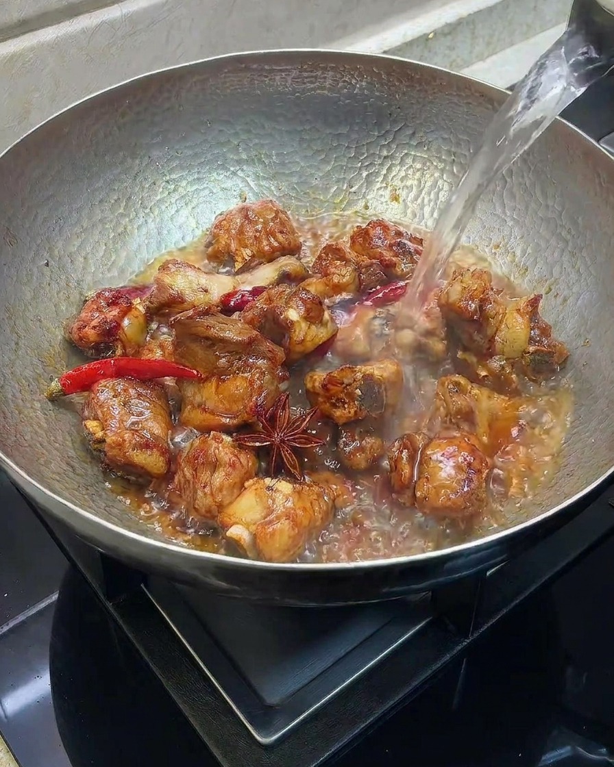Heißes Wasser wird in einen Wok mit angebratenen Rippchen und Gewürzen gegossen.