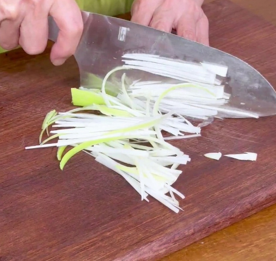 Fein geschnittene Frühlingszwiebelstreifen auf einem Holzschneidebrett, bereit für die Marinade.