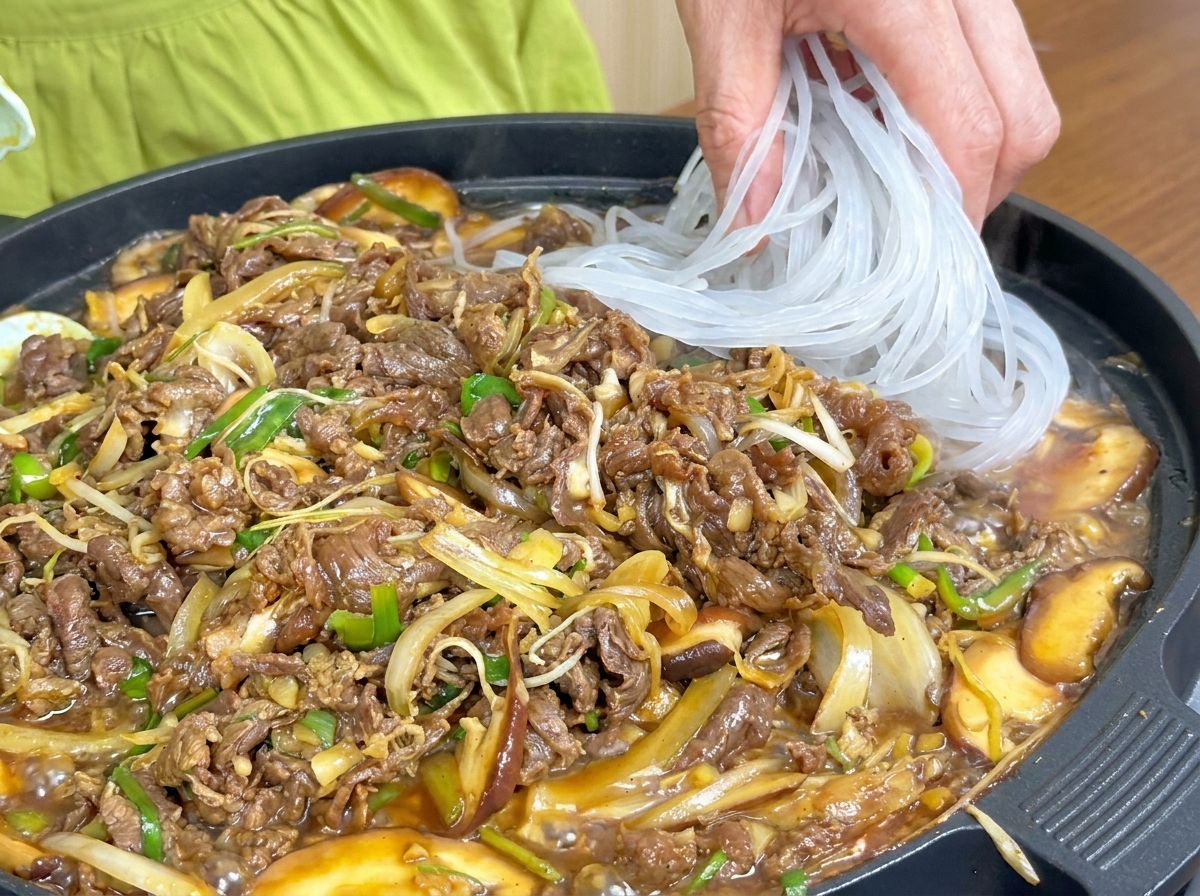 Durchscheinende Glasnudeln werden zu der Pfanne mit kochendem Fleisch und Gemüse hinzugefügt.