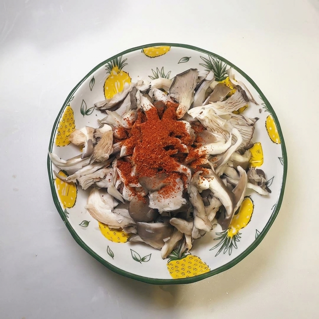 Ein Häufchen rotes Chilipulver liegt auf den ausgedrückten Pilzstreifen in der Schüssel.