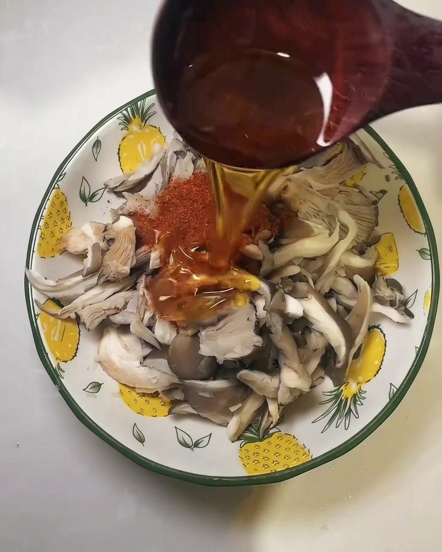 Speiseöl wird aus einem Holzlöffel über die gewürzten Pilze gegossen.