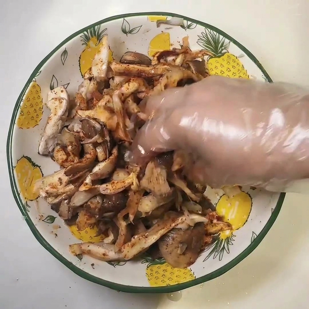 Eine Hand im Plastikhandschuh vermengt die gewürzten Pilze in einer Schüssel.