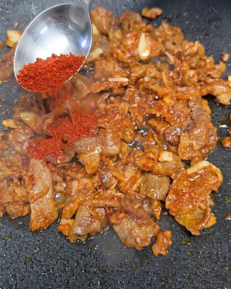 Rotes Chilipulver wird über die Rindfleischmischung gestreut.
