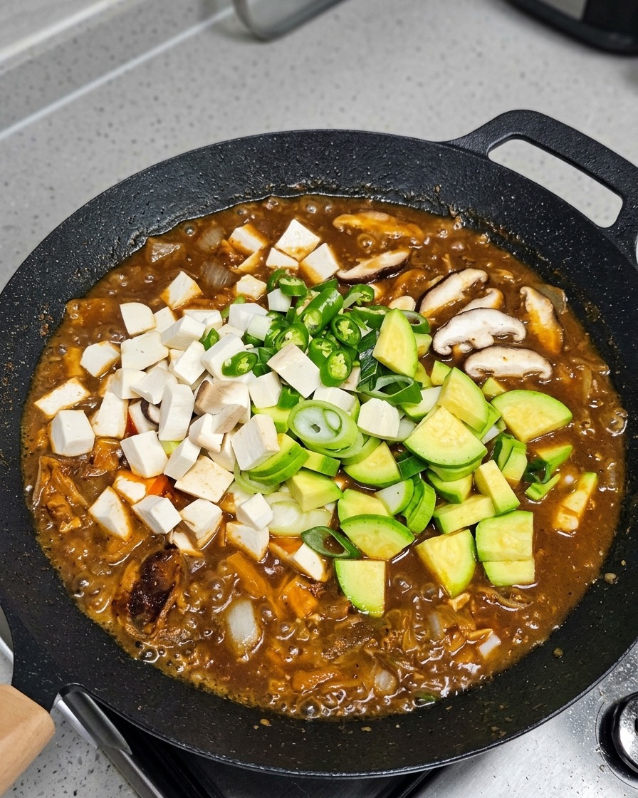 Gemüse und Tofu werden in den köchelnden Eintopf gegeben.
