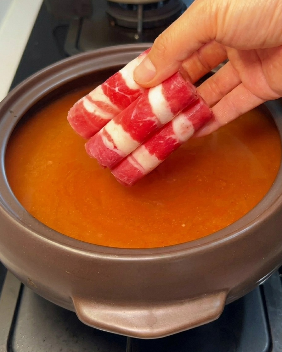 Dünn geschnittene, gerollte Scheiben von fettem Rindfleisch werden zur köchelnden roten Brühe gegeben.