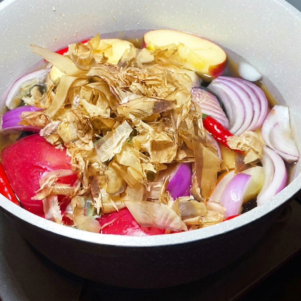 Getrocknete Bonito-Flocken werden in einen köchelnden Topf mit aromatischem Gemüse und Obst gegeben.