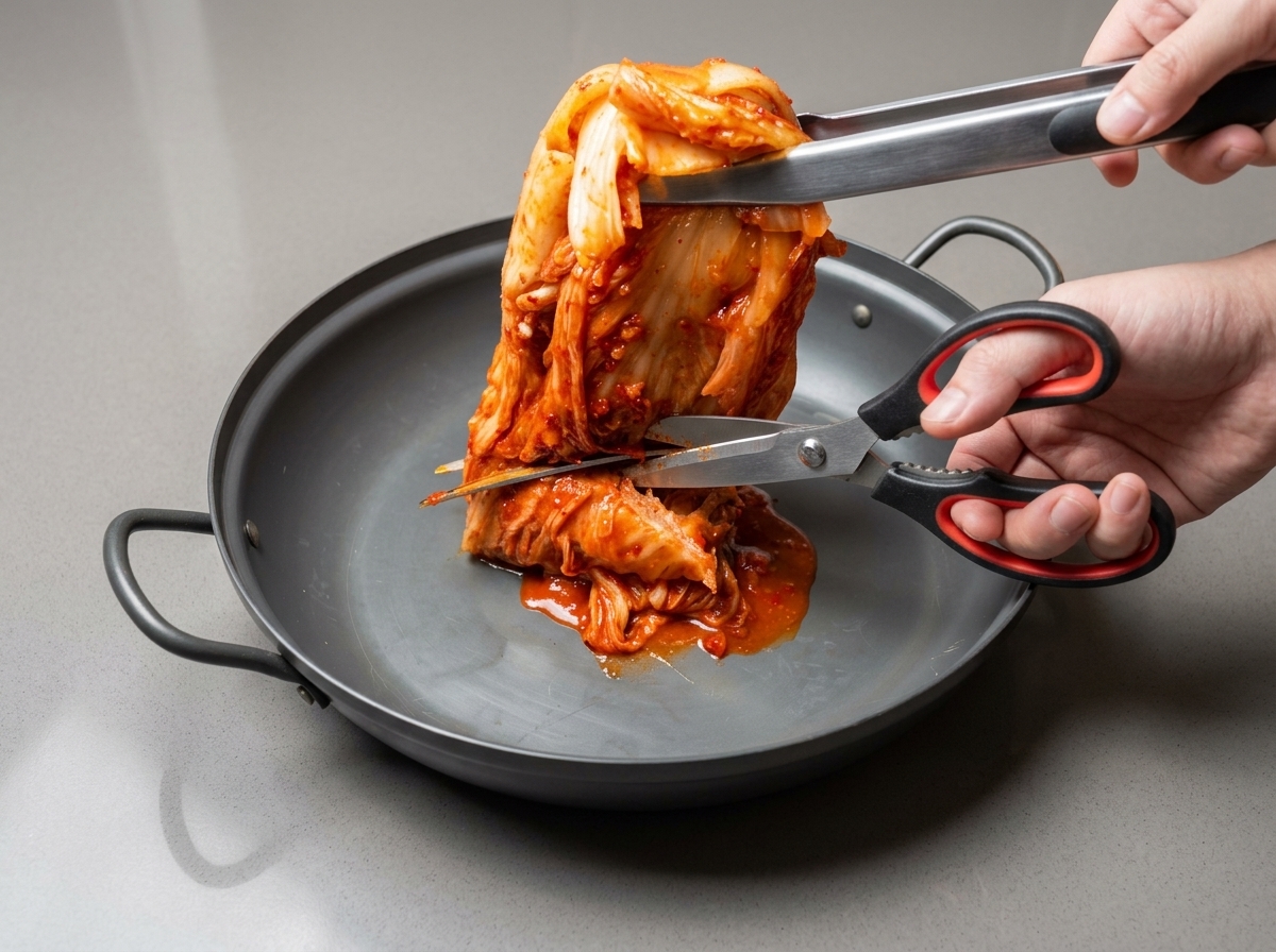 Küchenschere schneidet ganzen Kimchi direkt in einer großen Pfanne in mundgerechte Stücke.