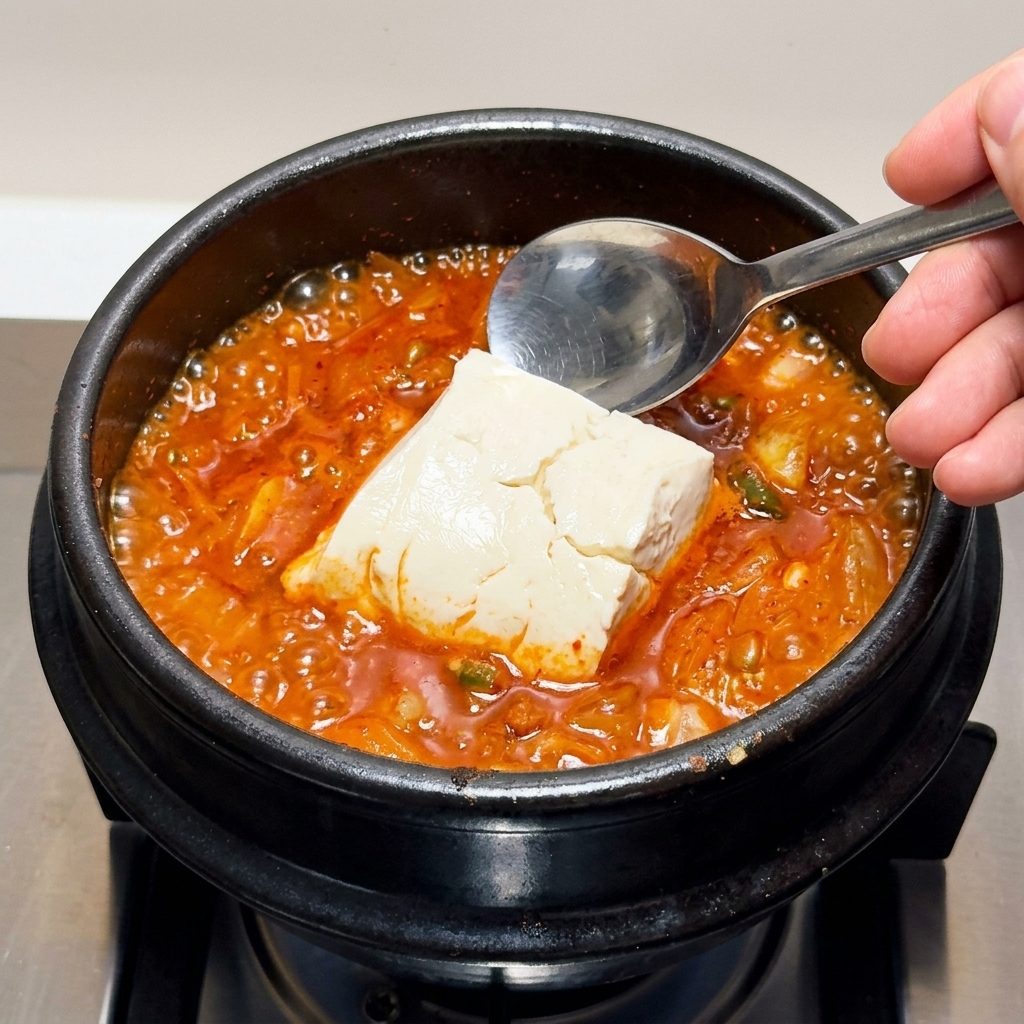 Große Stücke weicher Seidentofu werden vorsichtig in den kochenden Kimchi-Eintopf gehoben.