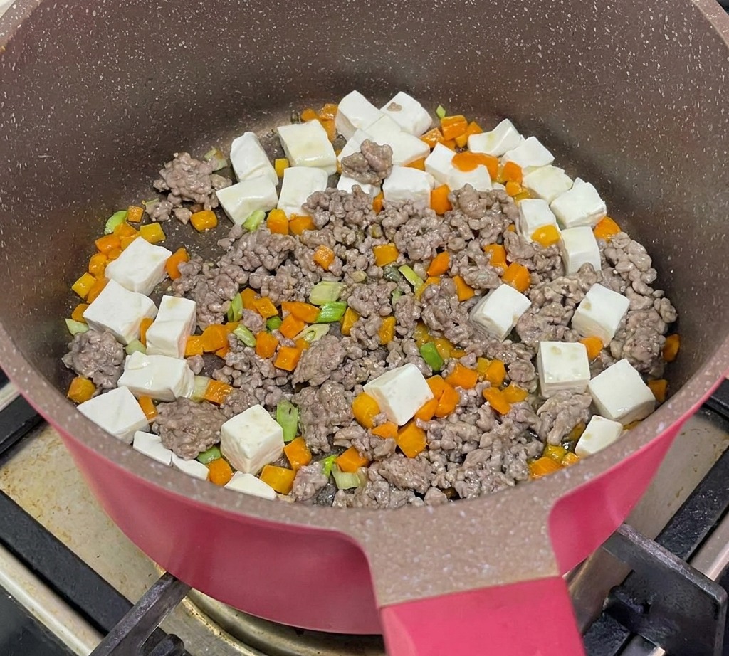 Kochendes Wasser wird in die Pfanne mit Tofu, Rindfleisch und Karotten gegossen.