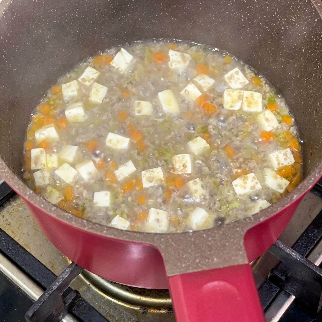 Sojasauce wird in den köchelnden Eintopf in der Pfanne gegeben.