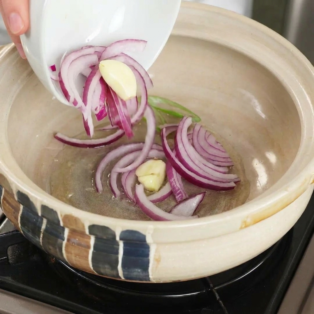 Zwiebeln und Knoblauch in einem erhitzten Tontopf mit Öl.