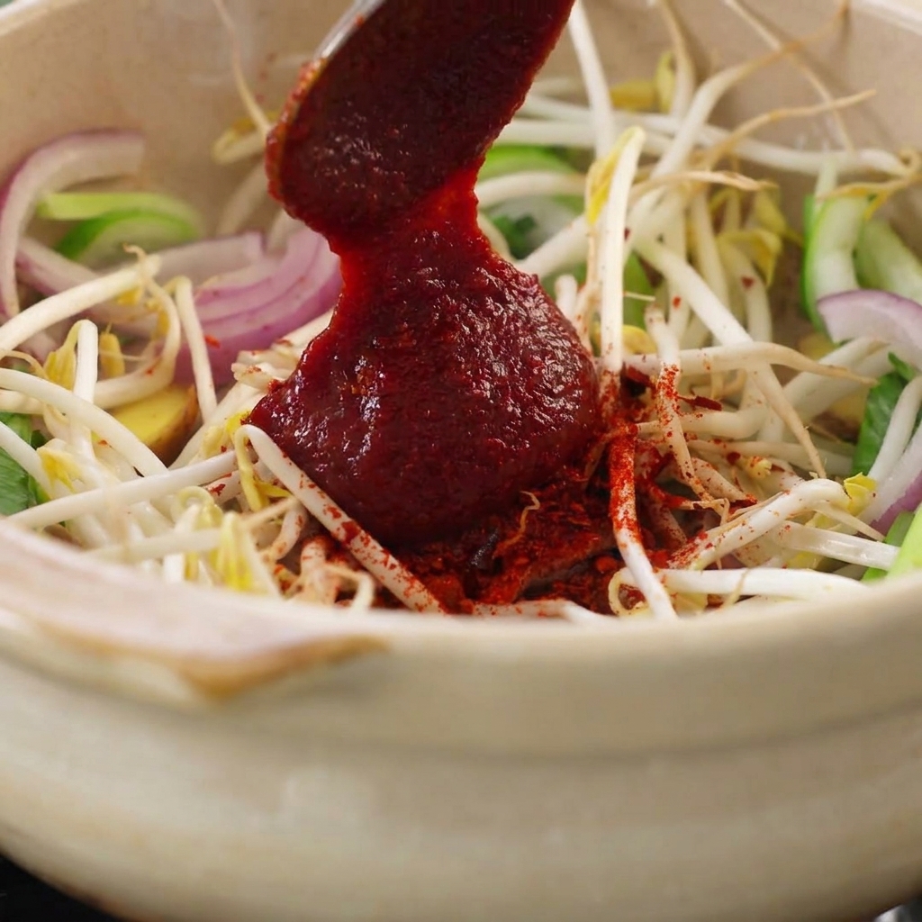 Ein Löffel rote Gochujang-Paste wird zur Gemüsemischung gegeben.