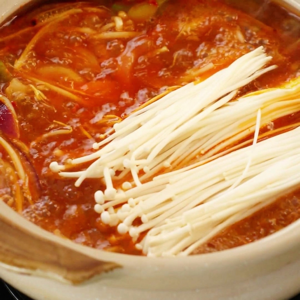Enoki-Pilze werden in die sprudelnde rote Brühe gegeben.