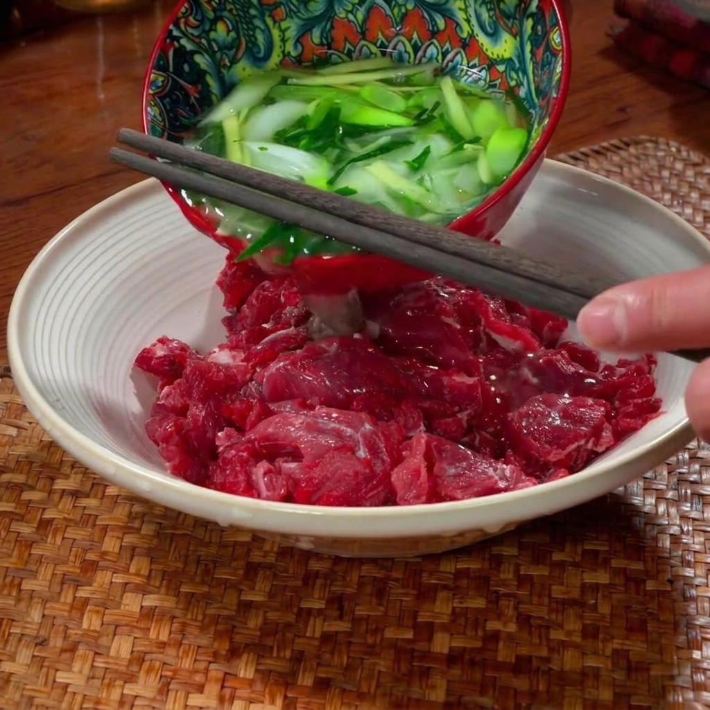 Dünn geschnittenes rohes Rindfleisch, das in einer Keramikschüssel gewürzt und von Hand massiert wird.