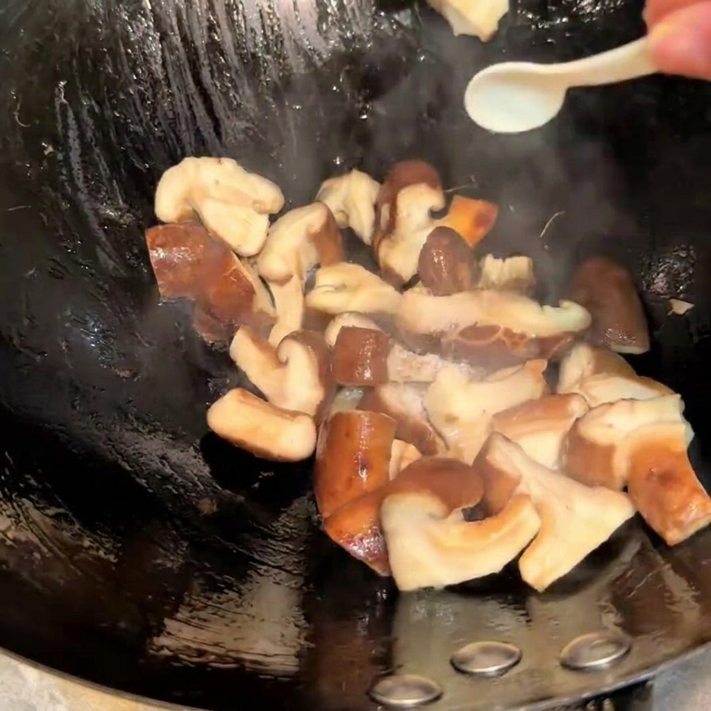 Würzende, rührgebratene Shiitake-Pilze in einem Wok mit Salz und Sojasauce unter Verwendung eines kleinen Löffels.