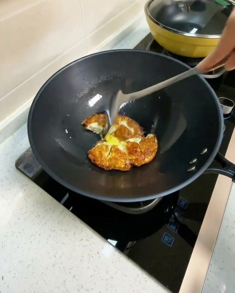 Heißes Wasser wird in einen Wok mit gebratenen Ei-Stücken gegossen.