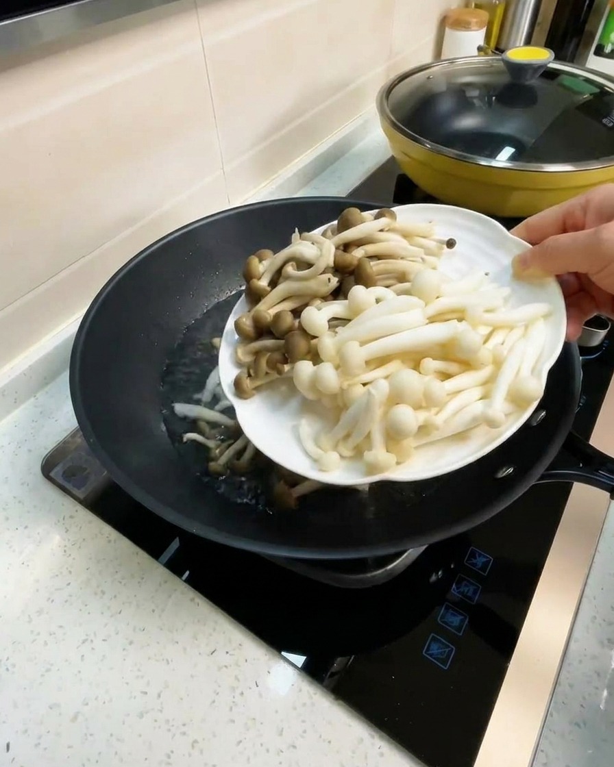 Ein Teller mit weißen Buchenpilzen und Crab-Flavored Pilzen wird zur kochenden Brühe gegeben.