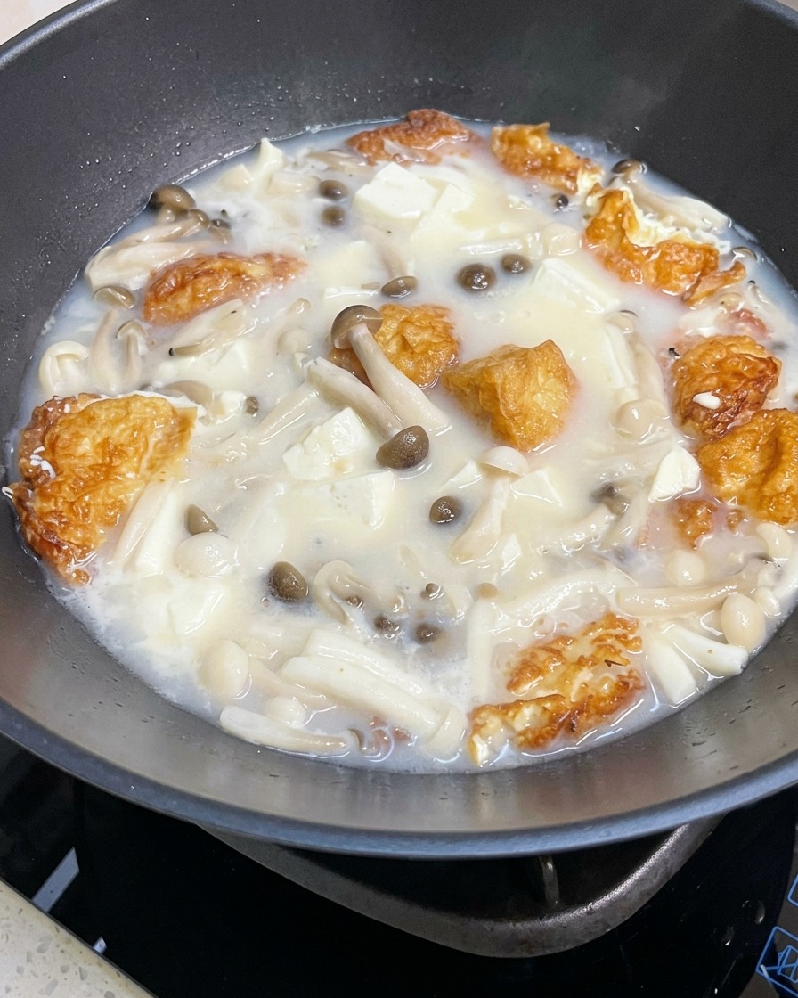Nahaufnahme der köchelnden Pilz-Tofu-Suppe, die mit Salz und Pfeffer gewürzt wird.