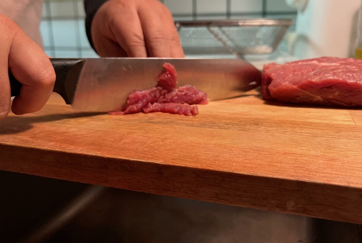 Mageres Schweinefleisch, das in dünne Streifen auf einem Holzbrett geschnitten wird.